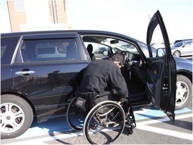 車いすドライバーが、自動車に乗るため、運転席のドアを全開にしている写真です。