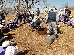 造園会社のかたを囲んで植樹の仕方を聞く小学生
